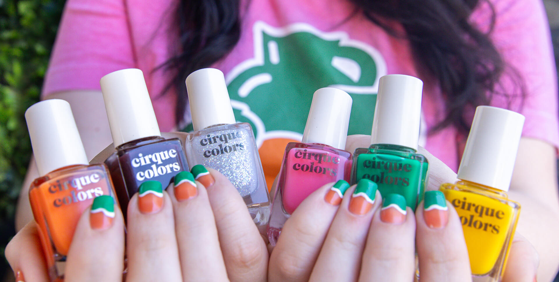 Close-up of hands holding Cirque Colors nail polish bottles in bold, vibrant shades inspired by Jarritos soda flavors. Featuring colorful nail art in orange, green, and white, this image showcases the playful collaboration between Cirque and Jarritos, celebrating Mexican flavor and creativity through nail design.