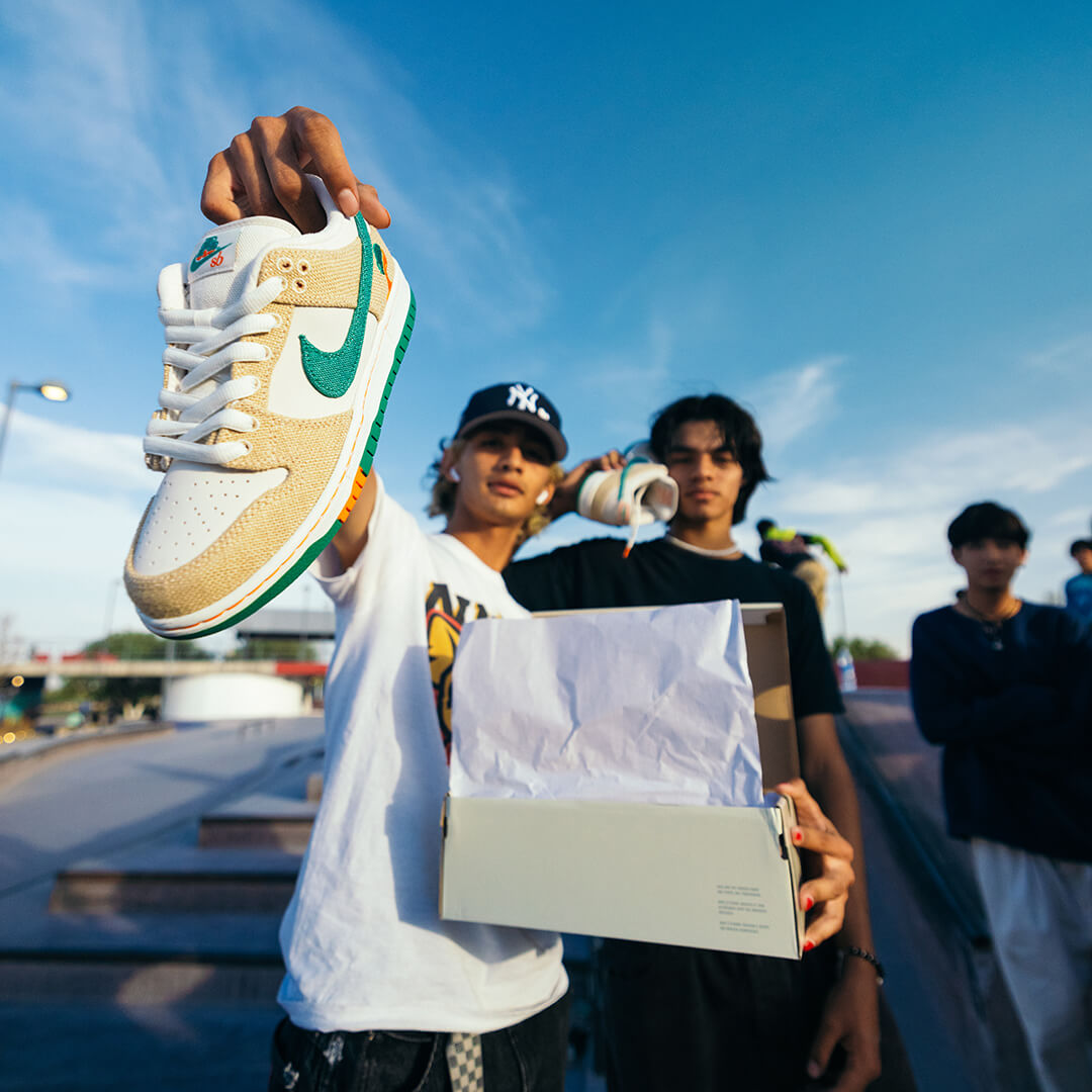 Two young men at a skatepark proudly showcase a limited-edition sneaker from the Nike and Jarritos collaboration, featuring vibrant green and orange accents inspired by the iconic soda brand—capturing streetwear culture and bold brand fusion.
