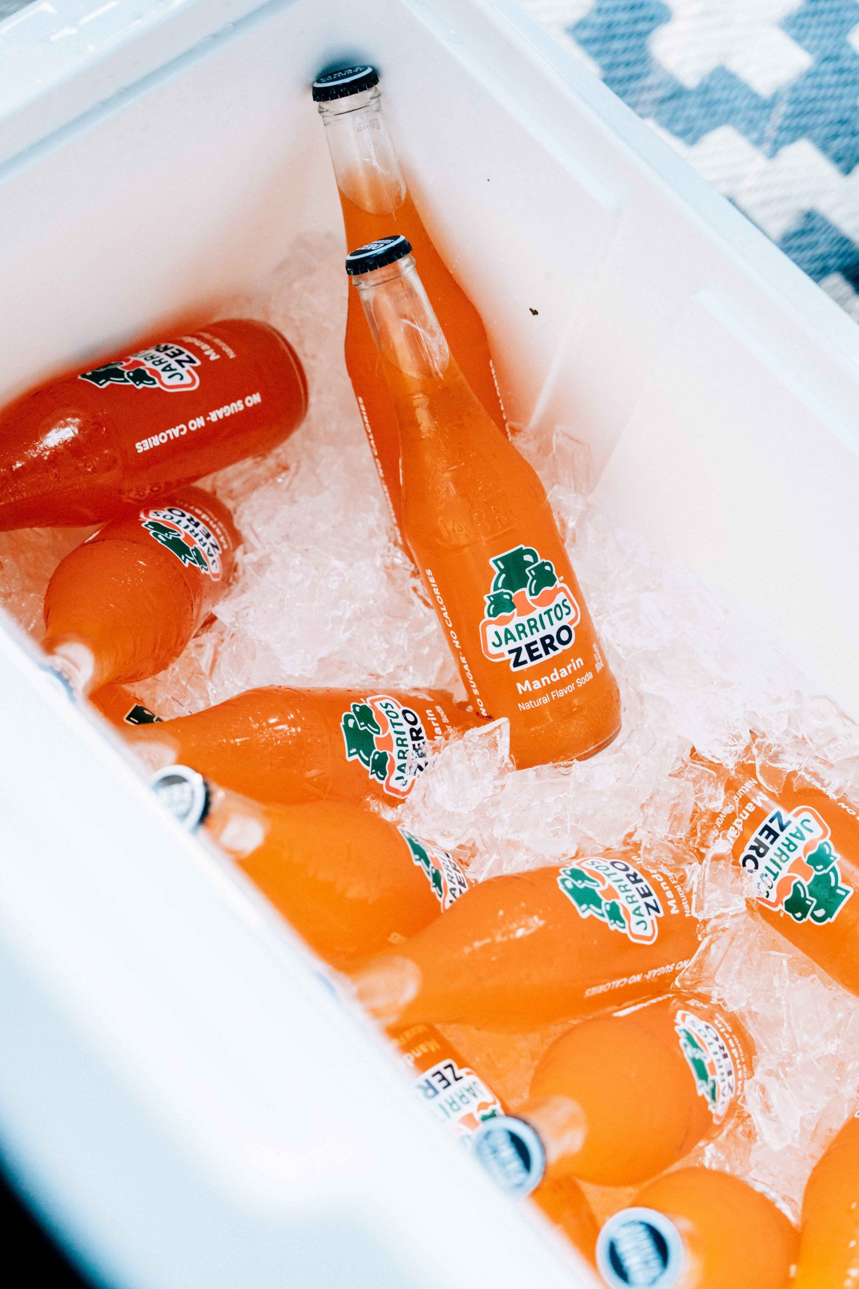 Multiple bottles of Jarritos Zero Mandarin soda chilled in a cooler filled with ice—highlighting the drink’s vibrant orange color, zero sugar formula, and refreshing appeal, perfect for outdoor gatherings or summer moments.