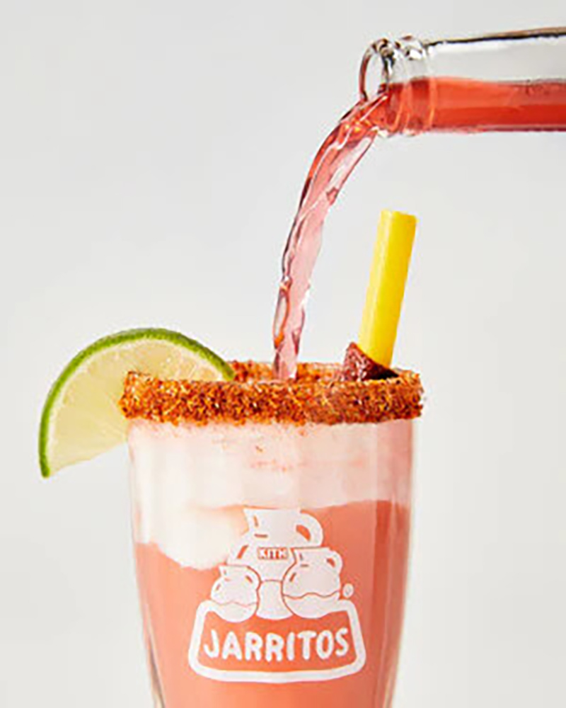 A refreshing pink Jarritos soda is poured into a chamoy-rimmed glass with ice, lime wedge, tamarind candy, and yellow straw. Featuring the Jarritos logo, this vibrant drink is part of a limited-edition collaboration with Kith Treats, blending bold flavor with creative style.